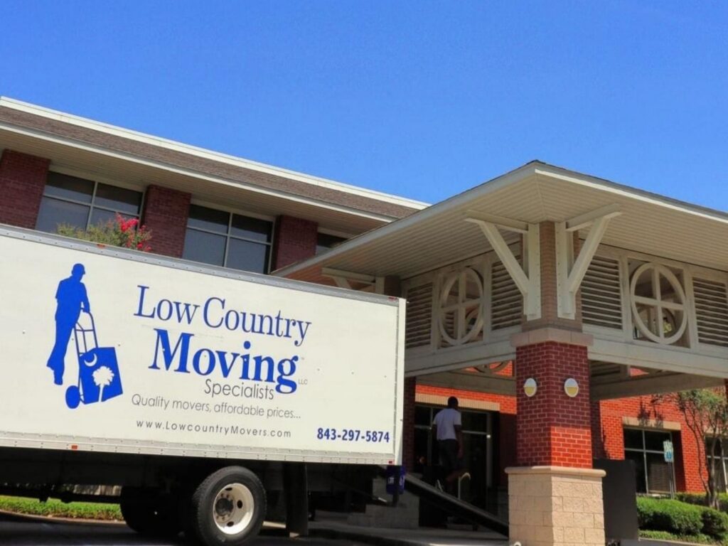 Low Country Moving Specialists box truck parked at the covered entrance of a brick building as a man walks to the door