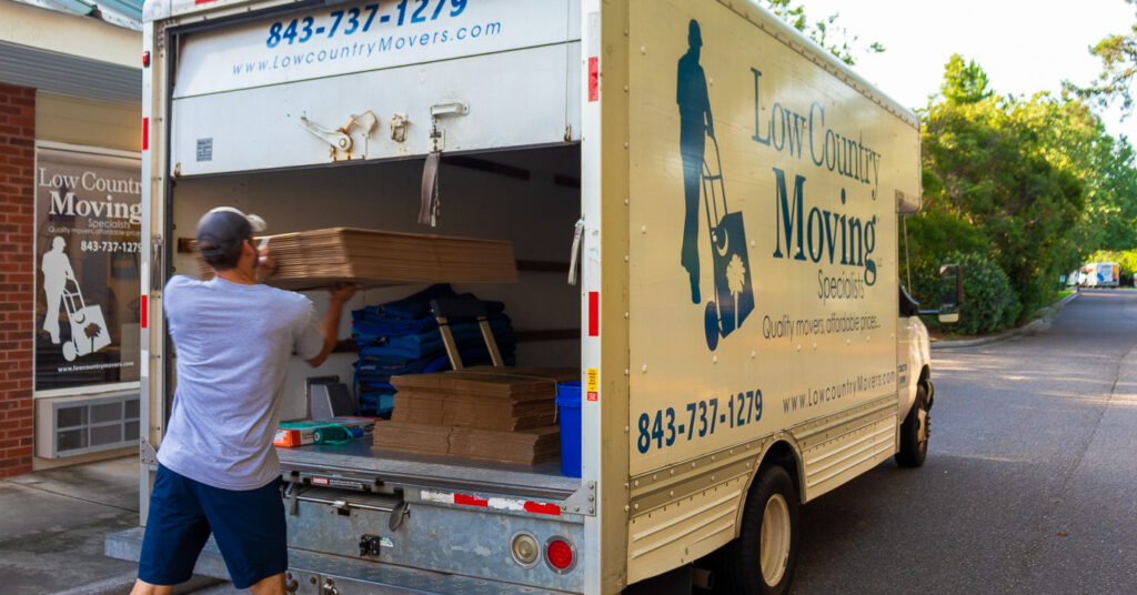 Low Country Moving Specialists crew member loading stacks of flat cardboard boxes into the back of a company truck