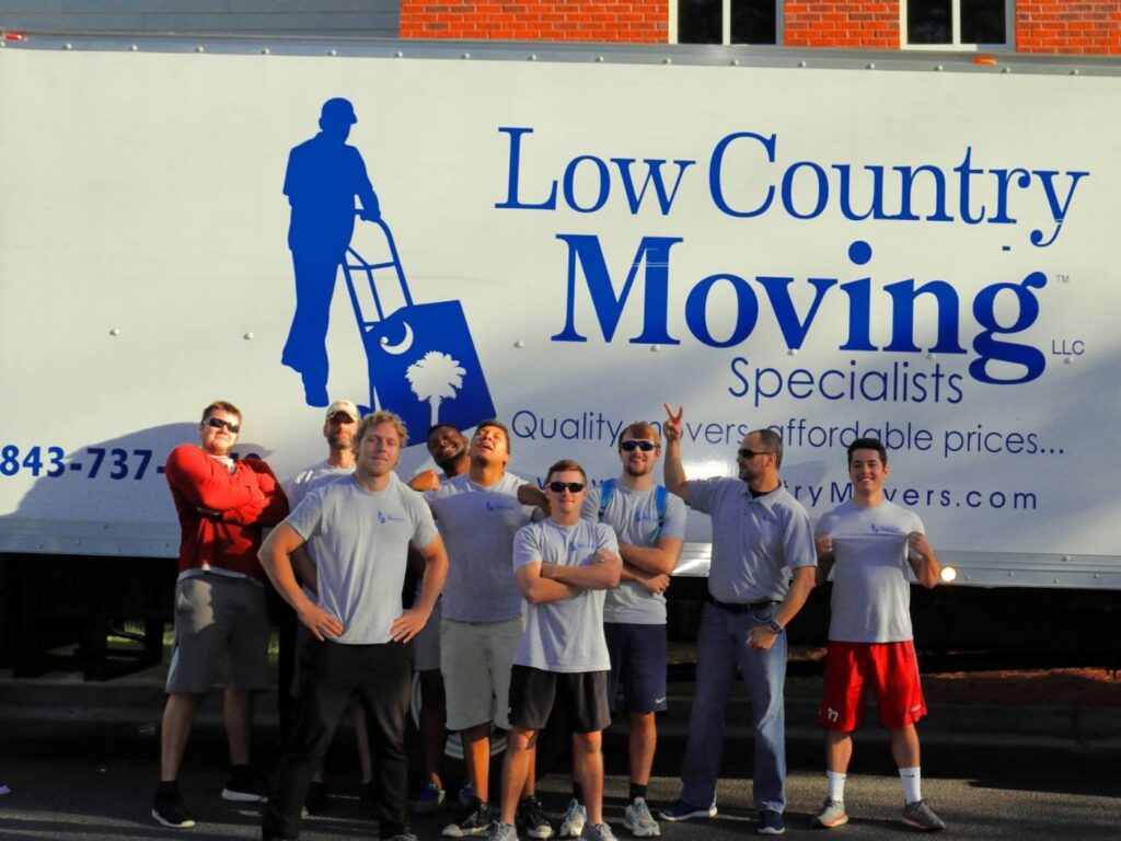 Nine Low Country Moving Specialists crew members posing in front of the company logo on a white moving truck